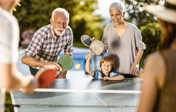 Happy extended family having fun while playing table tennis in the backyard.
